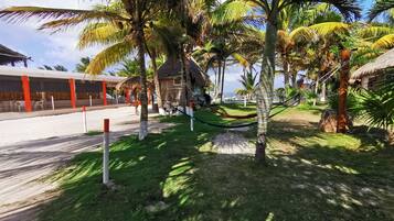 Un complexe hôtelier tropical avec des palmiers, un chalet au toit de chaume et une vue sur la plage.