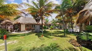Una località turistica tropicale con capanne a tetto di paglia, palme e un prato verde.