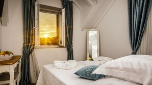 A hotel room with a bed, a window with curtains, a bedside table with a fruit bowl, and a mirror on the wall. - Heritage Hotel Dea Hvar (Hvar)
