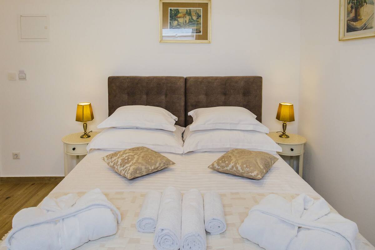 A neatly made bed with rolled towels, two bedside lamps, and a framed picture on the wall.