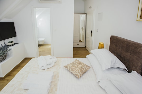 Un dormitorio con cama, televisión y baño a la vista a través de una puerta abierta.