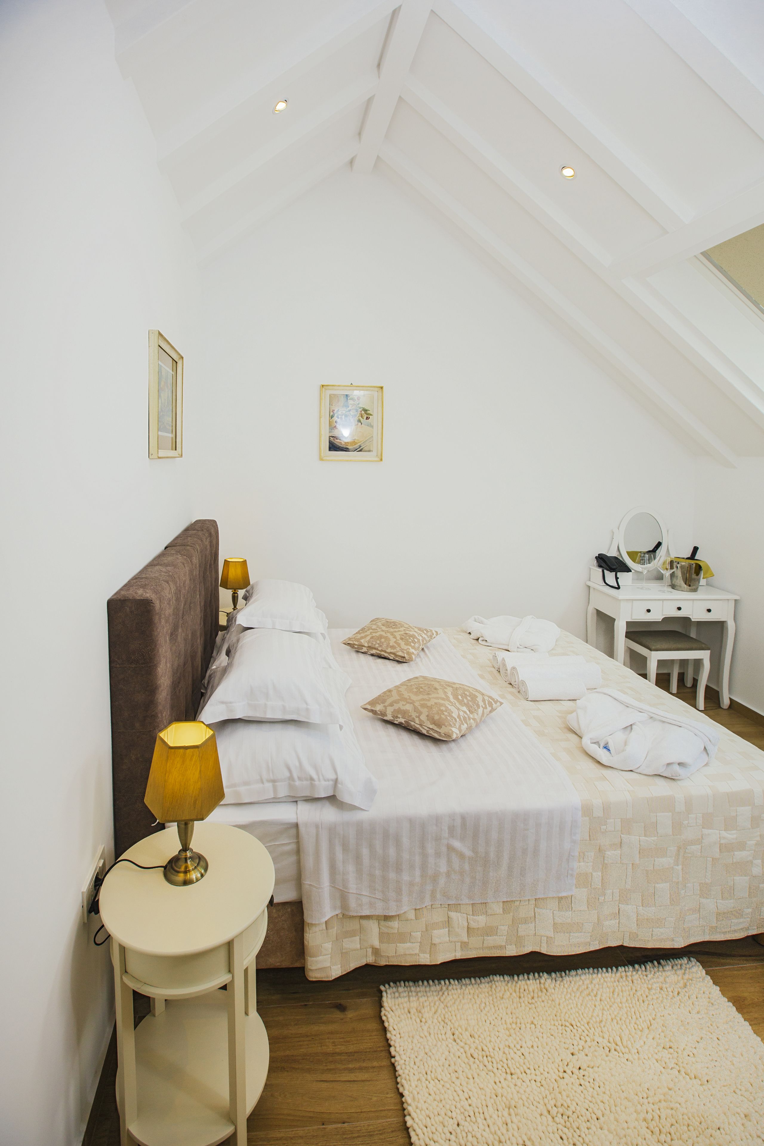 A bedroom with a bed, bedside table, lamp, and a desk with a mirror.
