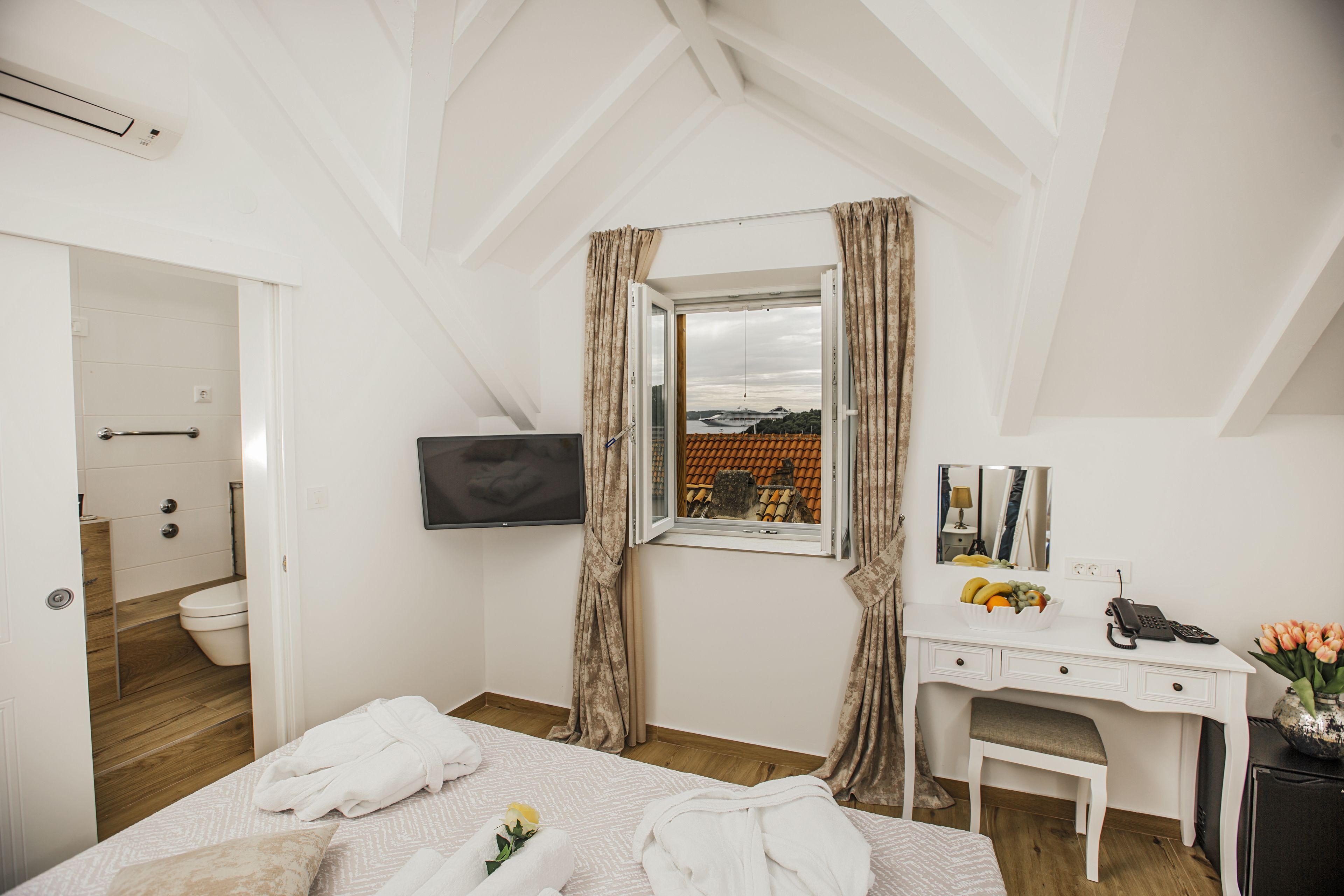 Une chambre à coucher avec un lit, un bureau, une chaise, une télévision et une fenêtre avec des rideaux.