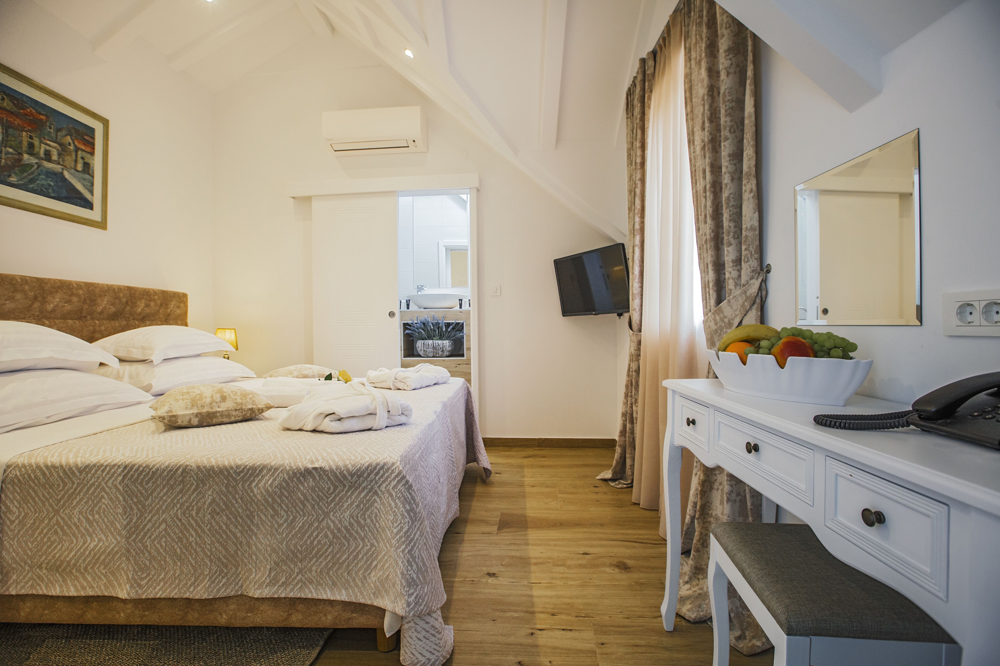 A hotel room with a bed, a bedside table with a bowl of fruit, a mirror, and a television.