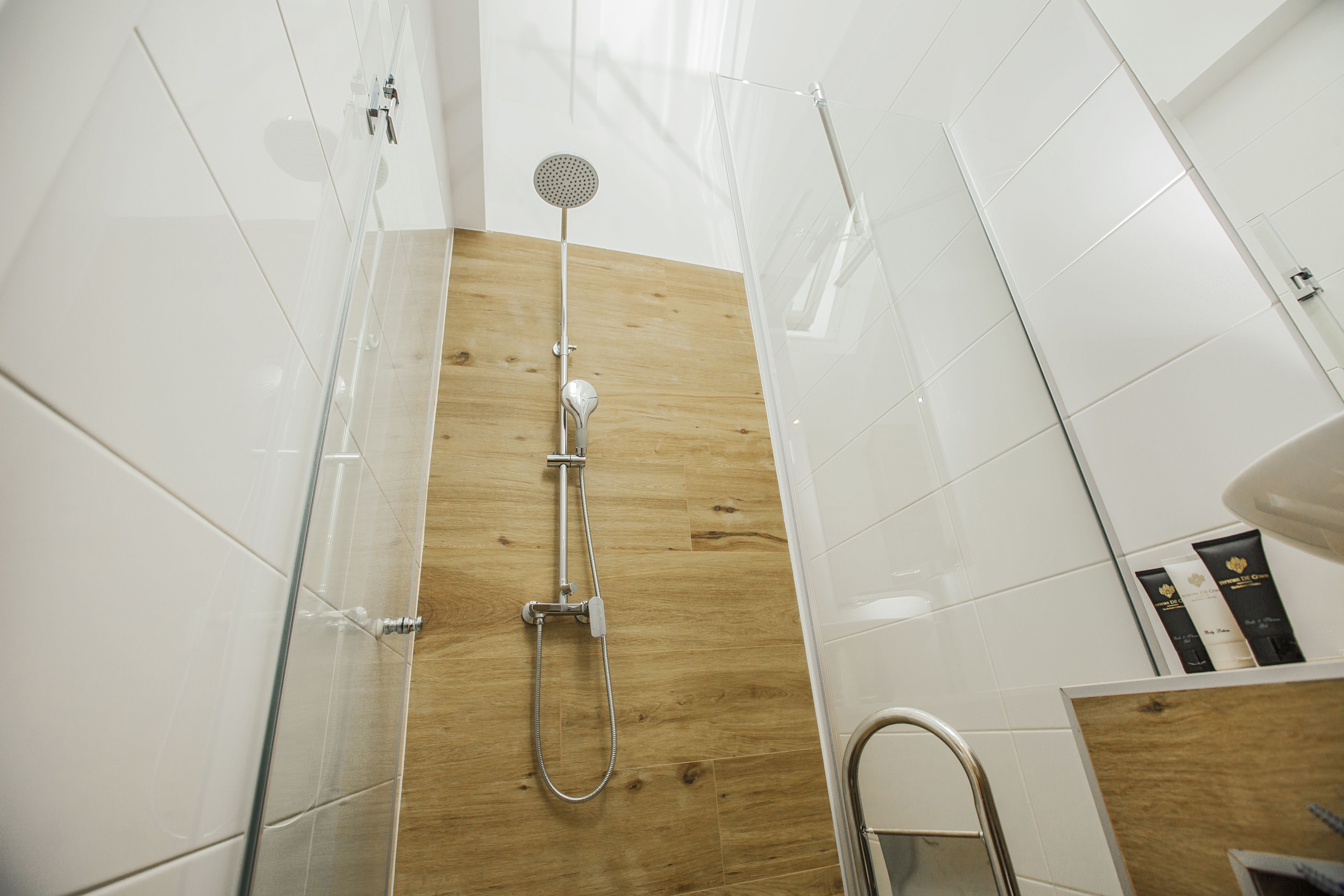 A modern bathroom with a shower, wooden panel wall, and white tiles.