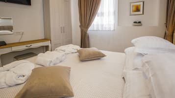A hotel room with a bed, pillows, a desk with a computer, a TV, and a window with curtains.