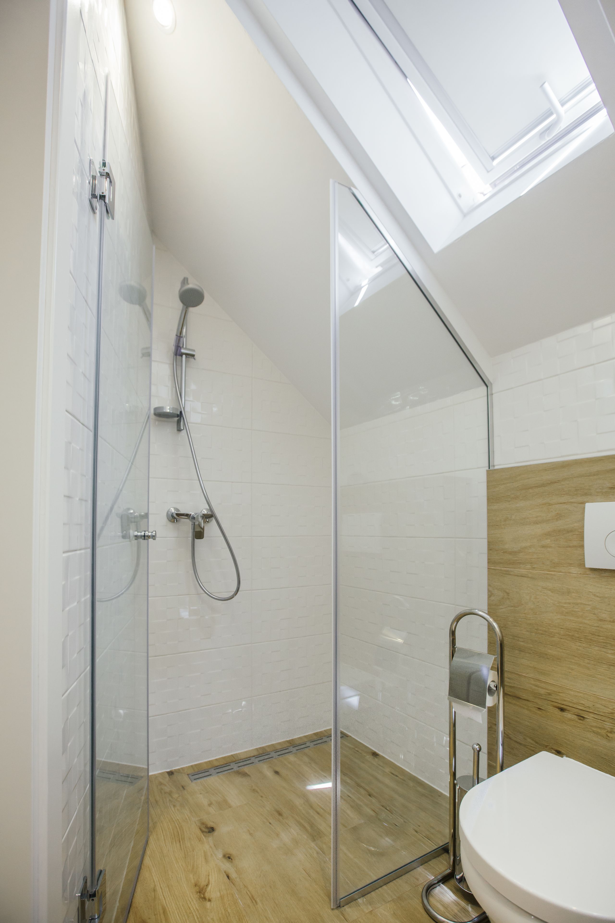 Un baño moderno con tragaluz, cabina de ducha de vidrio y suelo de madera.