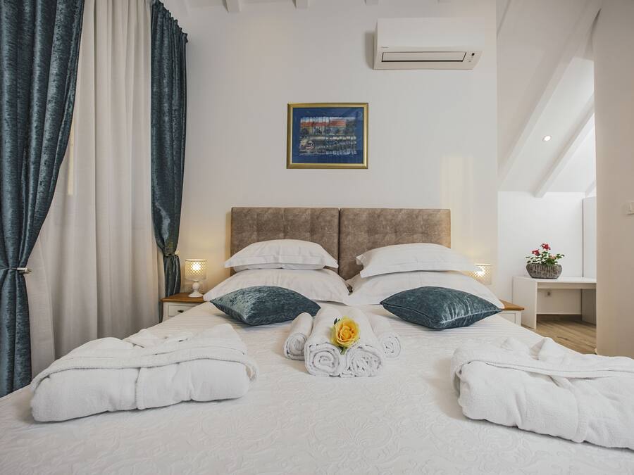 A neatly made bed with white linens, two pillows, and a rolled towel with a flower.