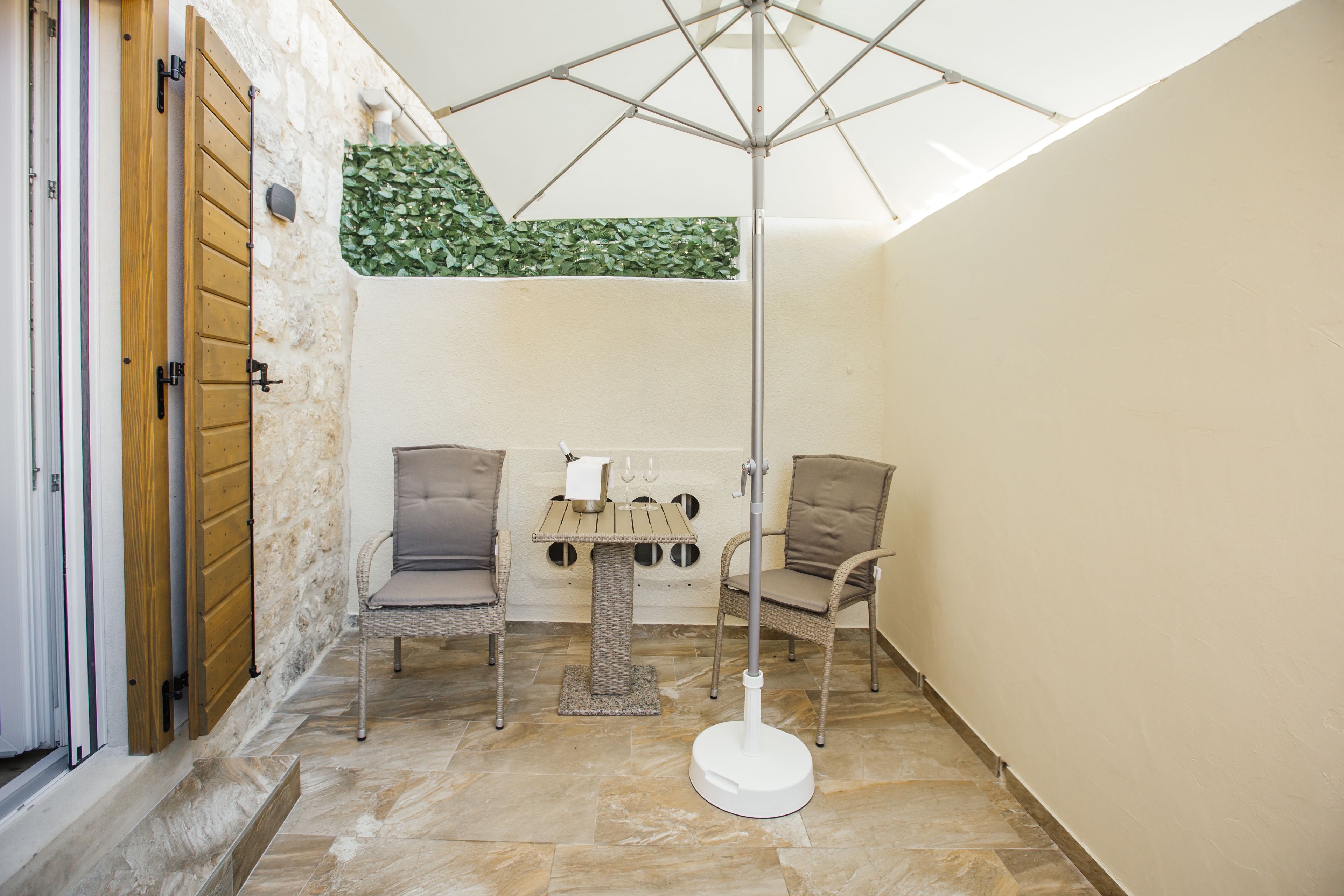 A small, enclosed patio area with a wicker table, two chairs, a floor lamp, and a ceiling fan.