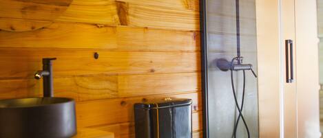 Een houten interieur met een douche in een glazen cabine, een zwart toilet en een plank met handdoeken.