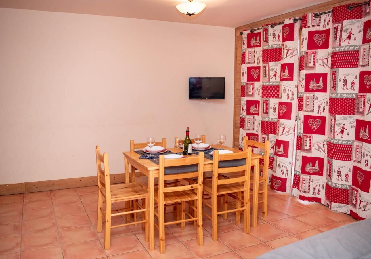 Un coin repas avec une table et des chaises en bois, une bouteille de vin et un téléviseur fixé au mur.