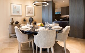 A dining area with a round table set for six, surrounded by six patterned chairs. There are framed artworks on the wall, a decorative sculpture, and a vase on a side table. - Luxury Sea View Apt in FIVE Resort on The Palm (Dubai)