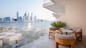 En moderne balkon med gelænder af glas, der giver udsigt over byens skyline og et vandområde.