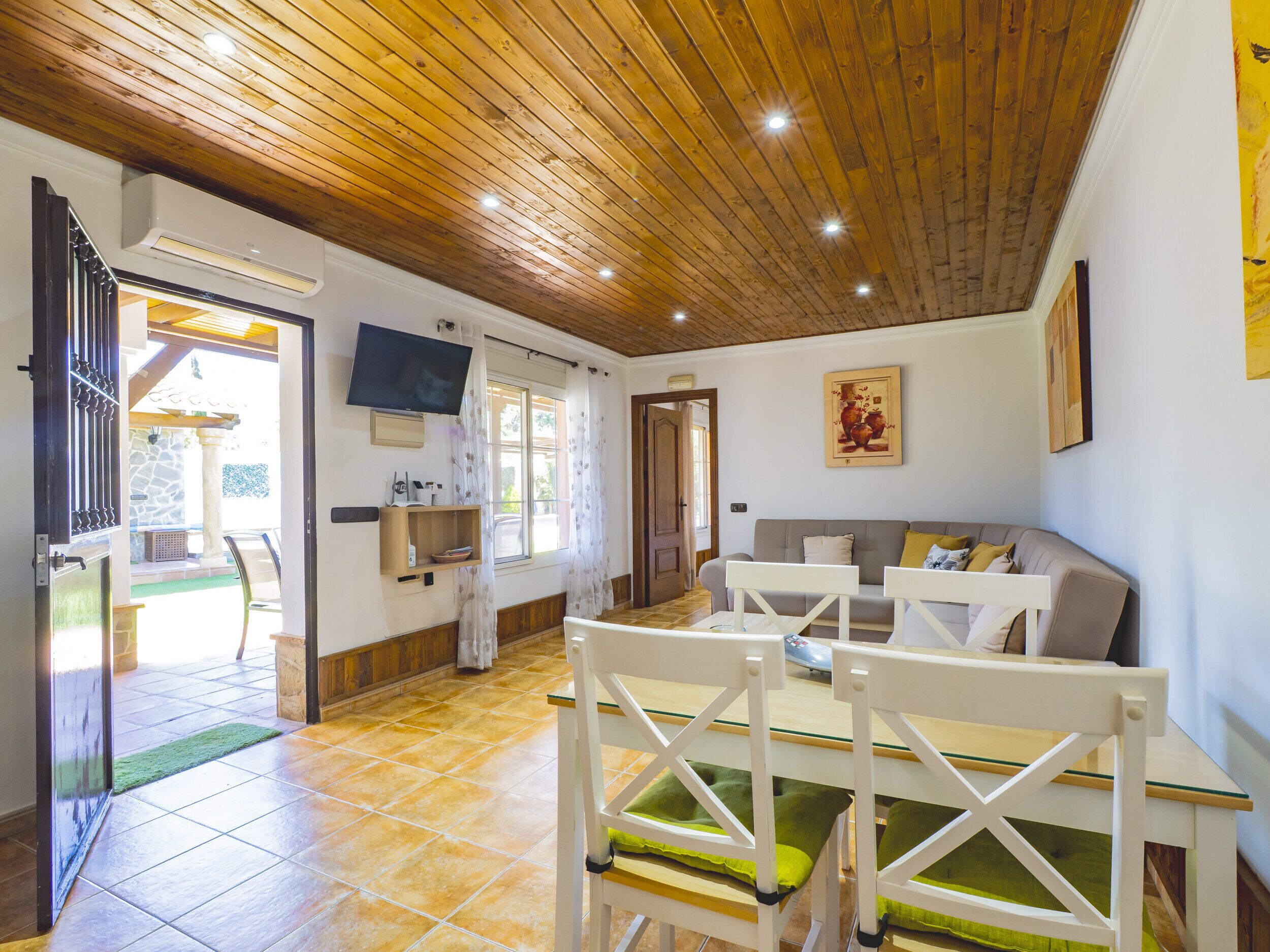 Una stanza accogliente con soffitto in legno, un divano, una TV e un'area pranzo con sedie e tavolo.