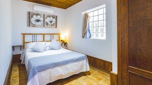 A bedroom with a wooden ceiling, a bed with white bedding, a nightstand with a lamp, a window with curtains, and a wooden door. - Cubo's Casa La Dehesilla High Privacy and Pool  / Private pool / free wifi (Alhaurín el Grande)