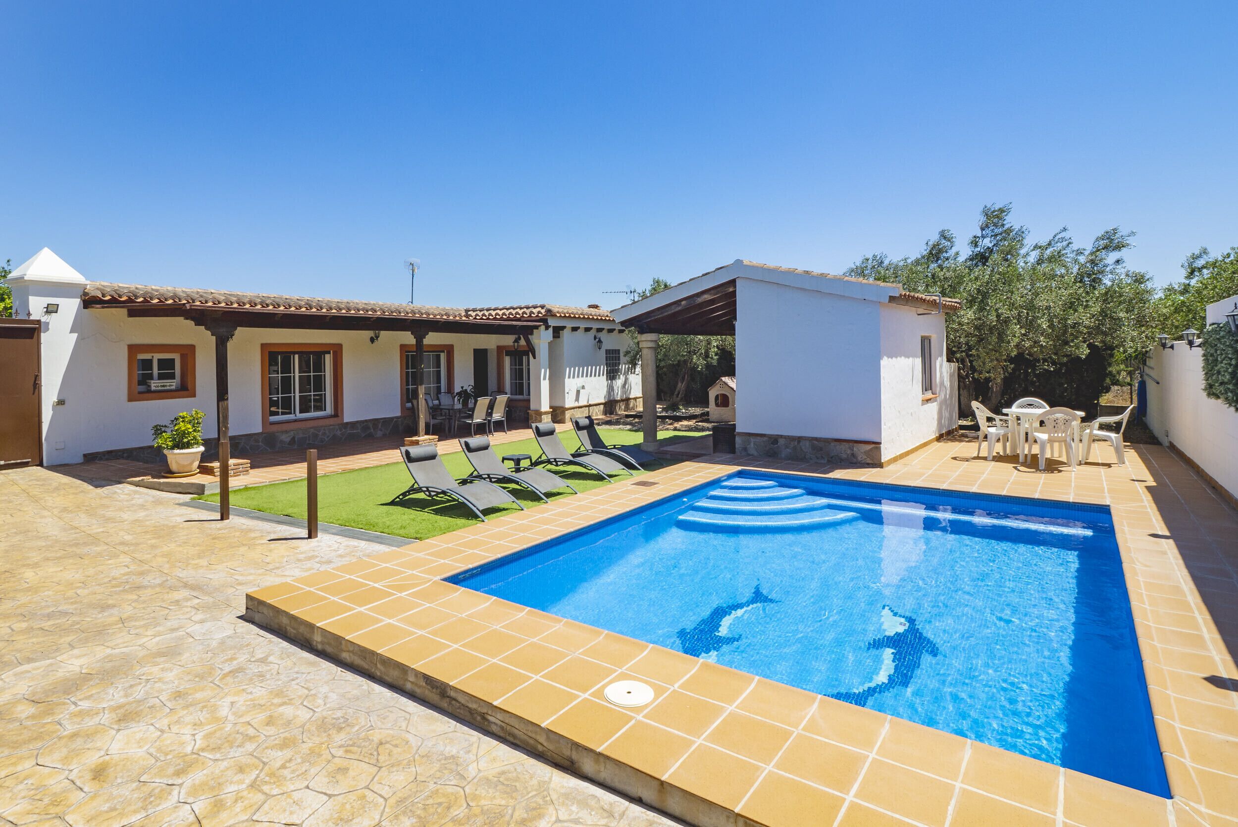 A swimming pool with a tiled deck, lounge chairs, and a small covered seating area.