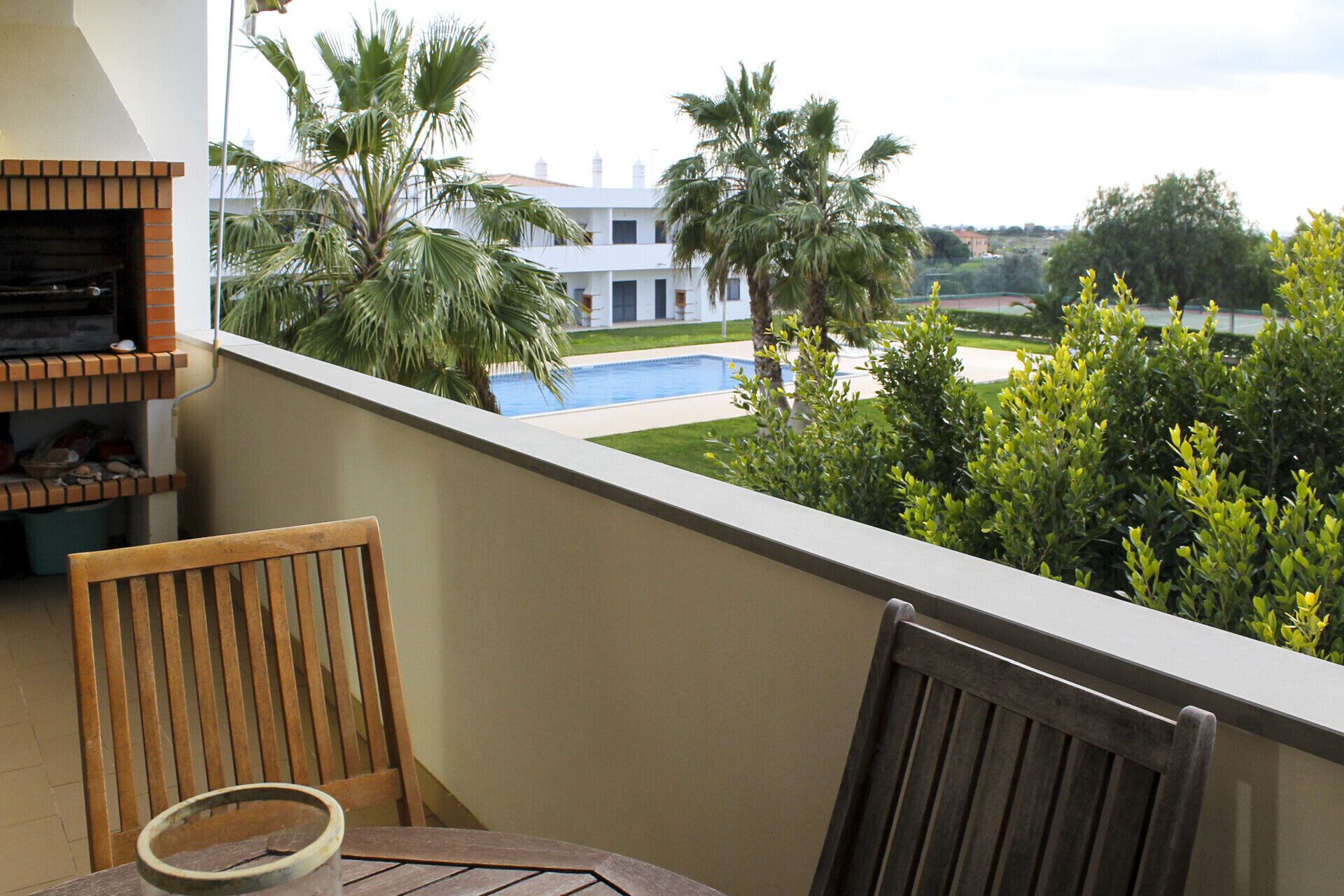 A balcony with a view of a swimming pool, palm trees, and a building in the background.
