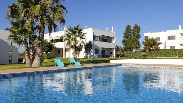A swimming pool with clear blue water, surrounded by palm trees and white buildings. - Condomínio Vilita, T1-Lt-5,F Pêra-Silves (Pêra)