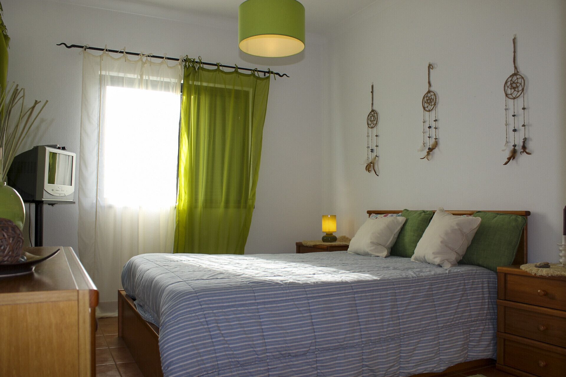 A bedroom with a bed, a nightstand, a lamp, a television, and wall decorations.
