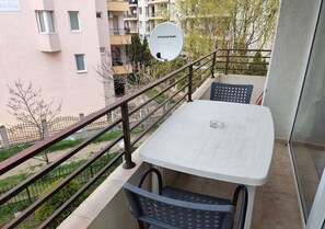 A balcony with a white table and two chairs, a satellite dish, and a view of a residential area with buildings and trees. - Charis Cozy Family Apart. at Sun Village  - ONLY 10 mins Walk to the Beach (Bourgas)