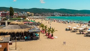 A beach with thatched-roof huts, beach umbrellas, and a clear view of the sea. - Charis Cozy Family Apart. at Sun Village  - ONLY 10 mins Walk to the Beach (Bourgas)
