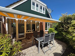 A house with a covered patio, a dining area with chairs, and a garden.