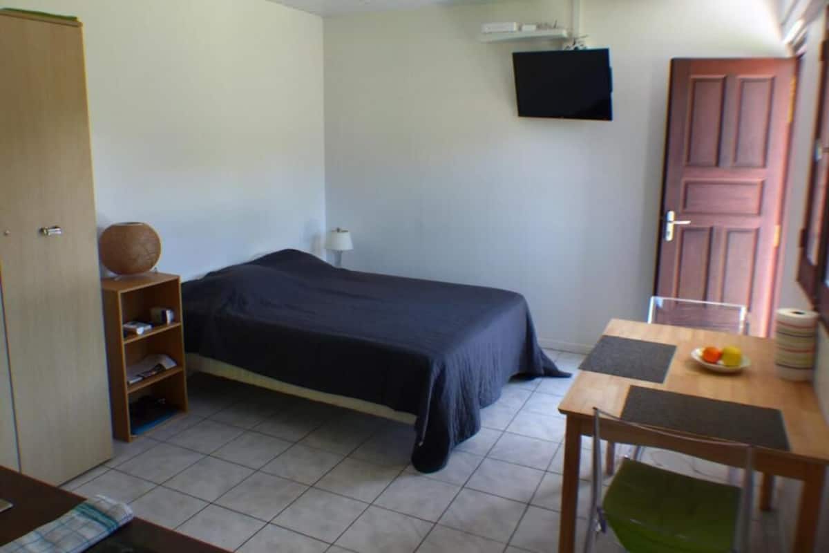 Une chambre à coucher avec un lit, un bureau et une chaise, un téléviseur fixé au mur et une porte.