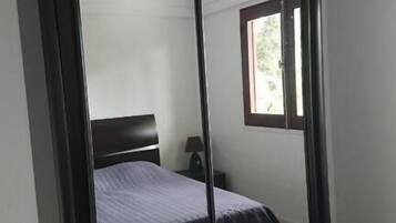 A bedroom with a bed, a nightstand, a window, and a wardrobe.