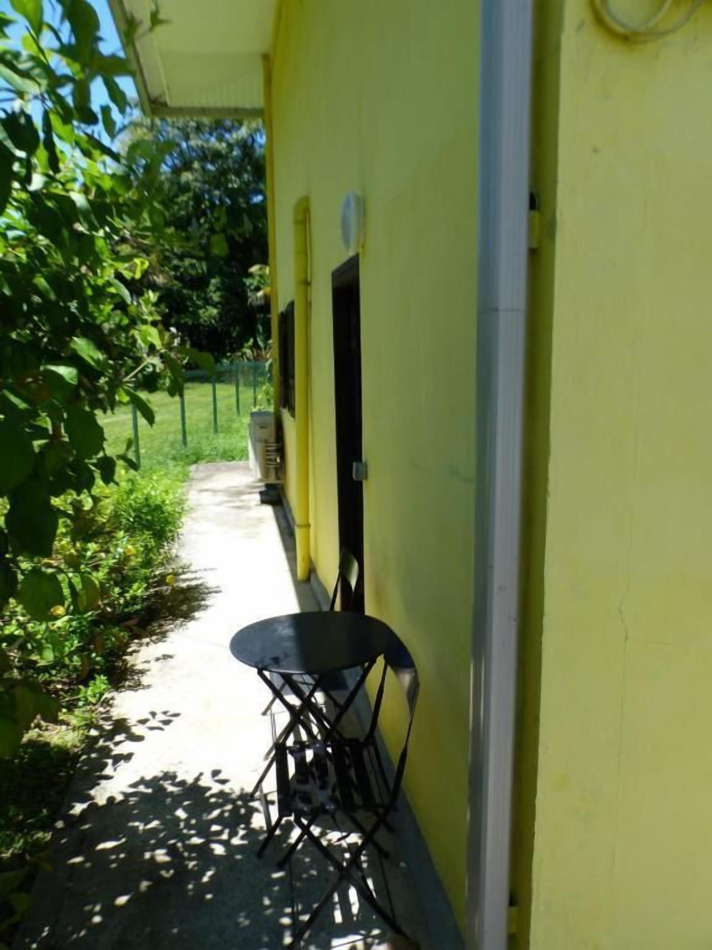 Un sendero estrecho que lleva a un edificio amarillo con una silla negra y una pequeña mesa.