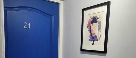 Una puerta azul con el número 21, un cuadro en la pared y un felpudo en la entrada.