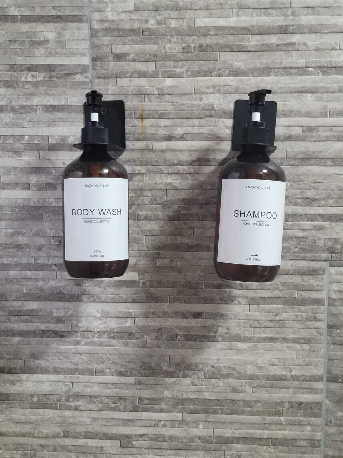 Deux bouteilles de gel douche et de shampoing sont accrochées à un mur dont le motif est constitué de briques.