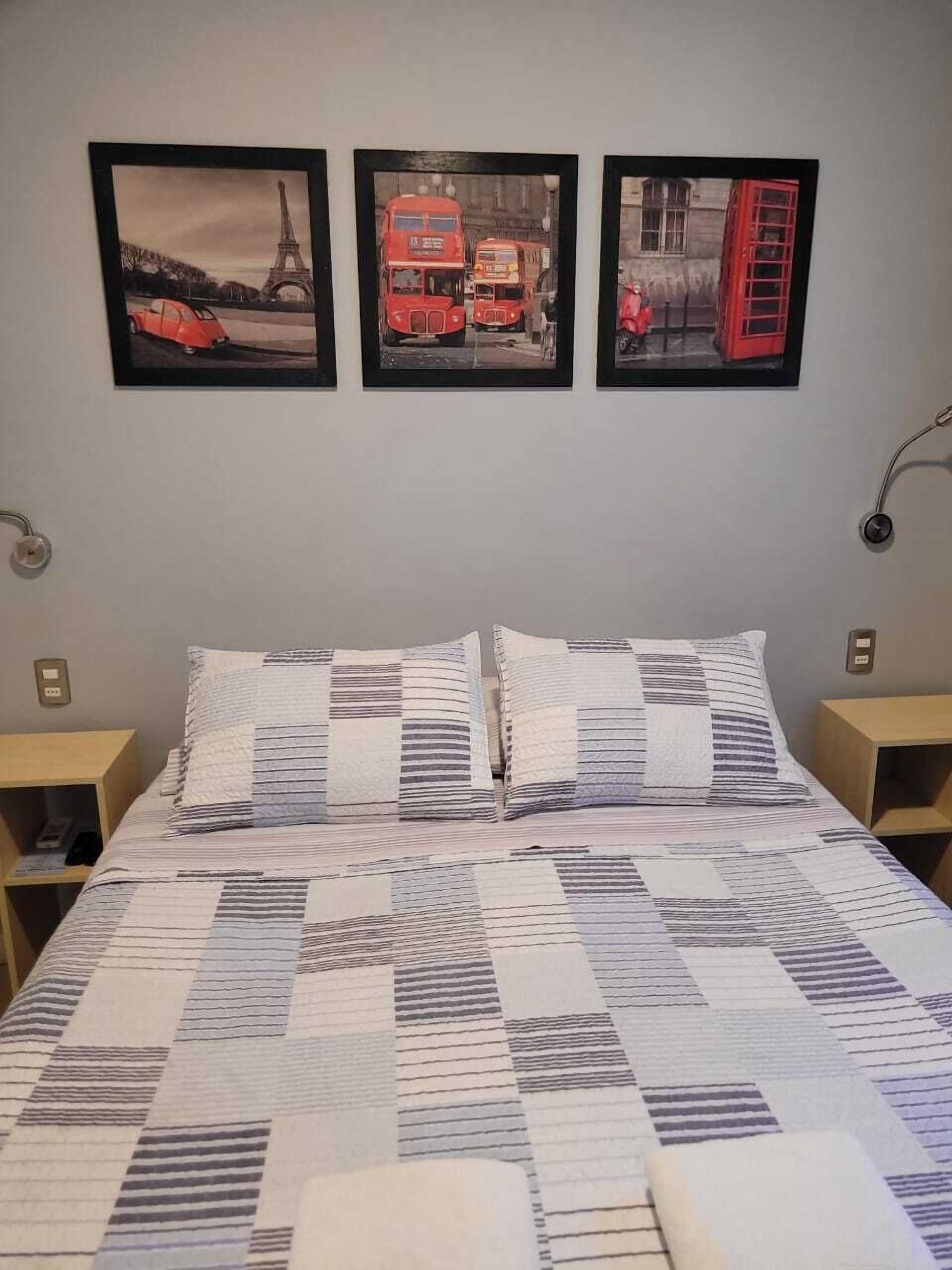 A bed with a quilt, two bedside tables, and three framed pictures on the wall.