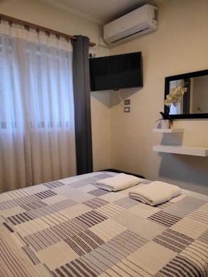 A hotel room with a bed, an air conditioning unit, a mounted TV, a mirror, and a small shelf with a vase. - Casa Marcoleta (Santiago)
