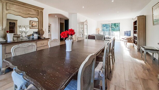 Une salle à manger spacieuse avec une longue table, des chaises et un vase rempli de fleurs rouges.