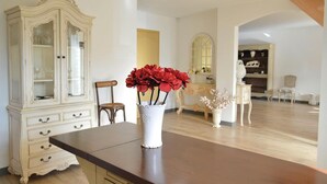 Une pièce comprenant une table à manger en bois, un buffet blanc aux portes vitrées, une chaise et un vase avec des fleurs rouges.