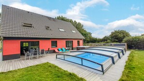 Une maison moderne dotée d’une piscine, d’une terrasse avec des chaises et d’un mur extérieur rouge.