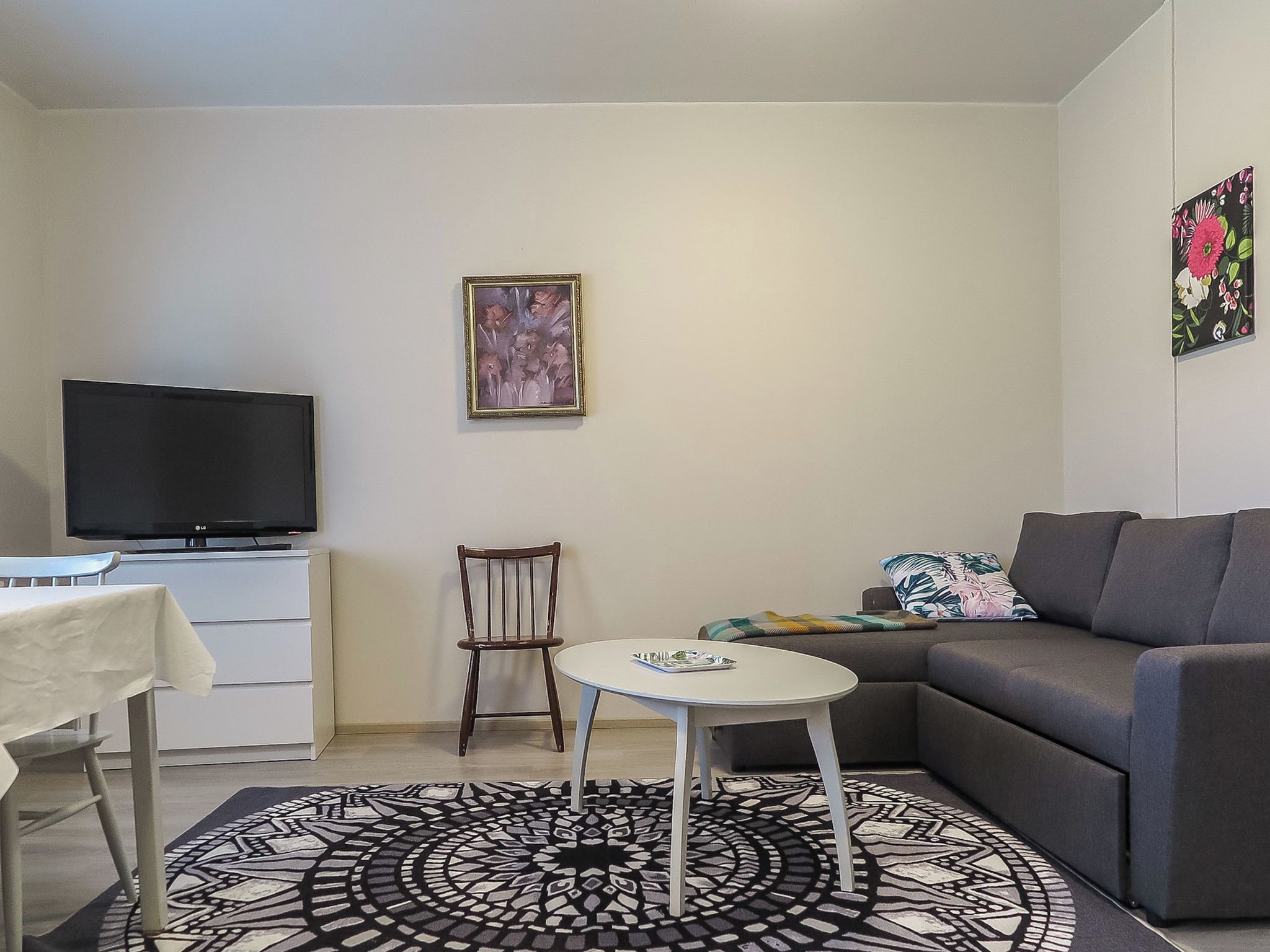 Ein Wohnzimmer mit Flachbildfernseher, einer Couch, einem kleinen runden Tisch, einem Sessel und einem gemusterten Teppich.