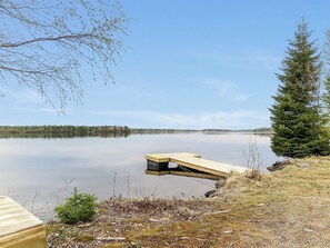 A calm lake with a wooden dock extending into the water, surrounded by trees and a clear sky.