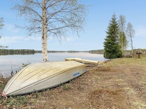 Un paisaje junto al lago con un bote, un árbol y un banco.