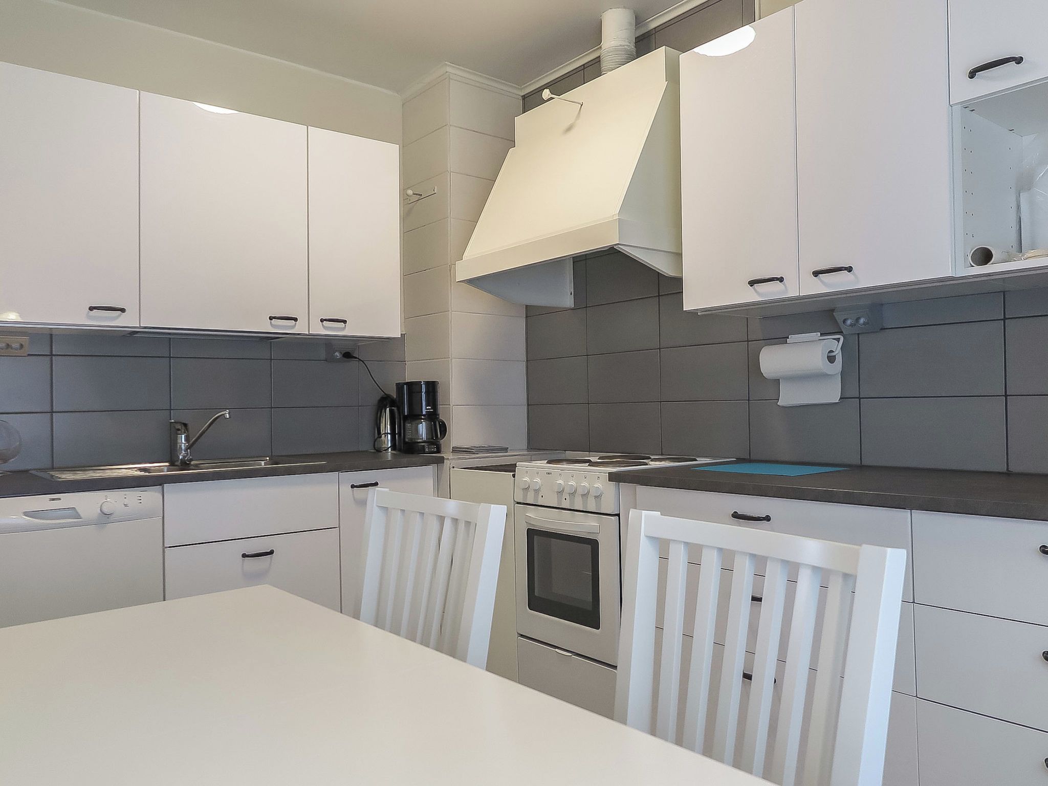 Une cuisine moderne avec des meubles blancs, une cuisinière et une machine à café.