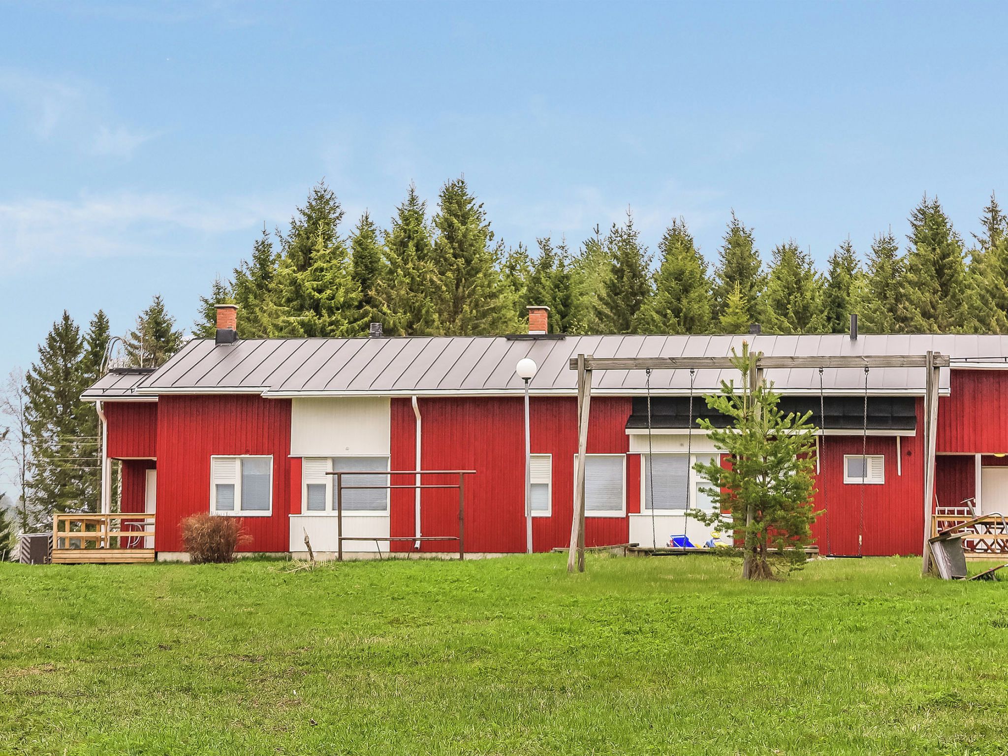 A red building with a metal roof, surrounded by green grass and trees.