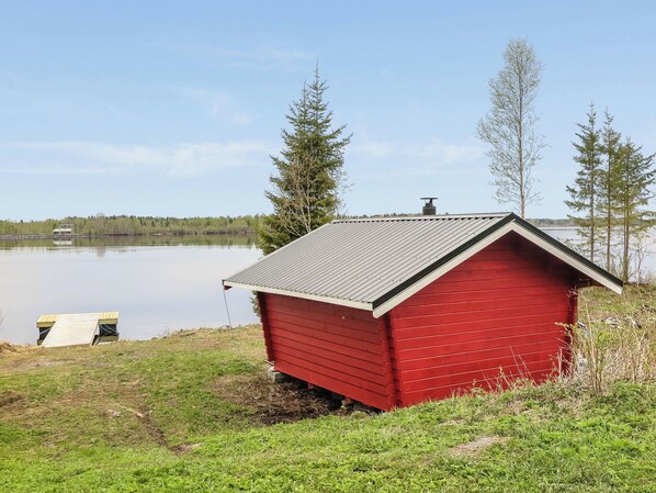 Una cabaña de madera roja junto a un lago, con cielo despejado.