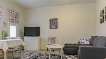 Una sala de estar con televisor de pantalla plana, una mesa de comedor, un sofá y un tapete estampado.