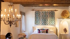 A cozy bedroom with a large bed, a chandelier, a patterned tapestry, and a wicker basket.