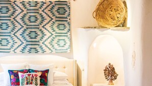 A cozy bedroom with a bed, pillows, a bedside table, and a small decorative item on a shelf.