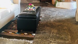 A spacious living room with a large sofa, a black ottoman, a wooden cabinet, and a large vase.