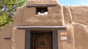 A rustic building with a wooden door, a small window with a bell, and a sign above the door.