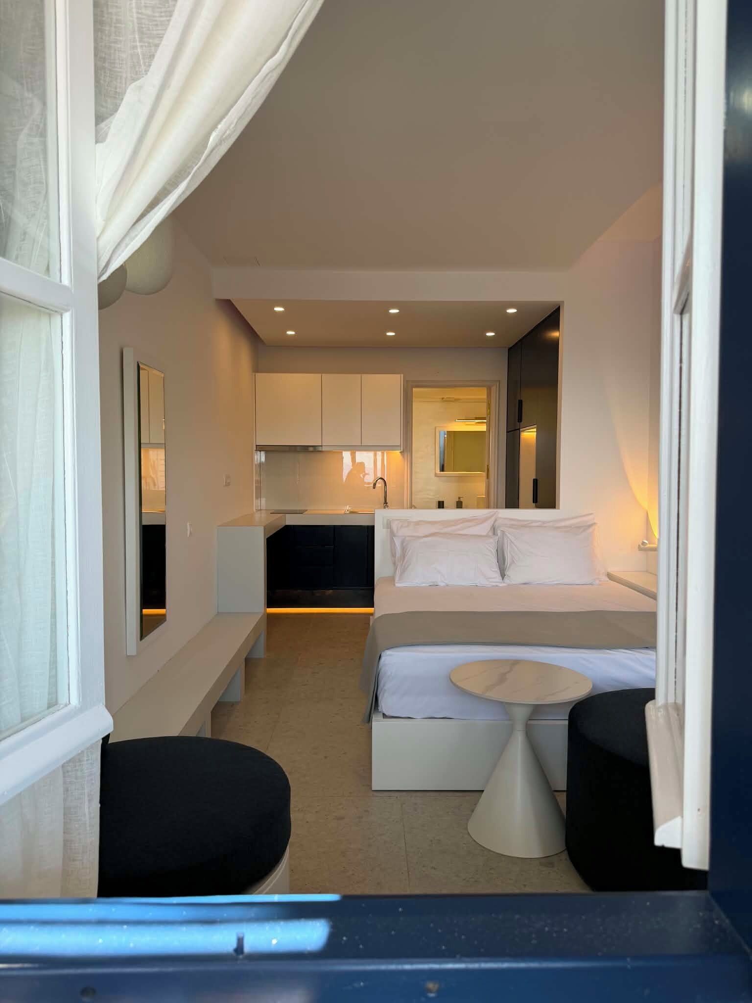 A compact hotel room with a bed, bedside table, and a small kitchenette.