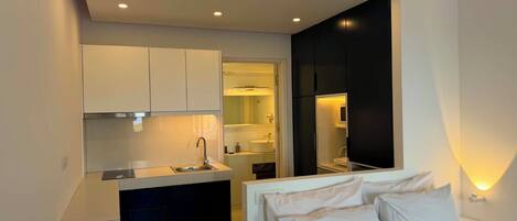 Un dormitorio compacto con cama, una kitchenette pequeña y un baño visible a través de una puerta abierta.