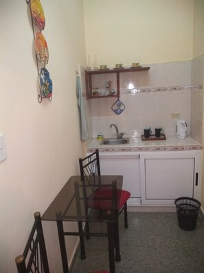 A small kitchen with a sink, a stove, and a microwave. There is a dining table with chairs and a black trash bin. - Casa Nidia Hab Indep (Havana)